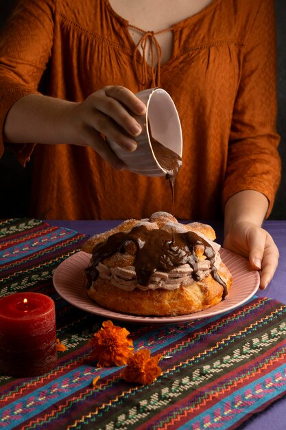 High angle of woman decorating pan de muerto with chocolate syrup